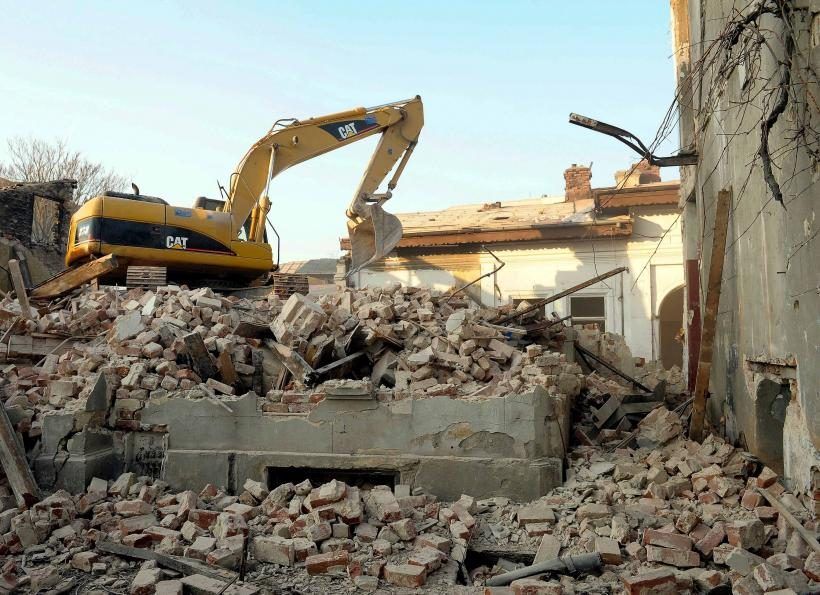 CAT excavator on brick rubble next to a partly demolished old building and basement walls